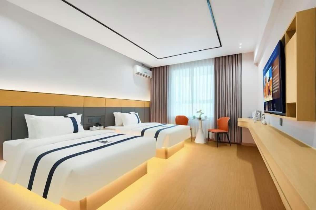 Habitación de hotel con dos camas, un escritorio, una silla, una mesita y un televisor.