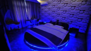 A modern bedroom with a circular bed, a patterned wall, and a hanging chair.
