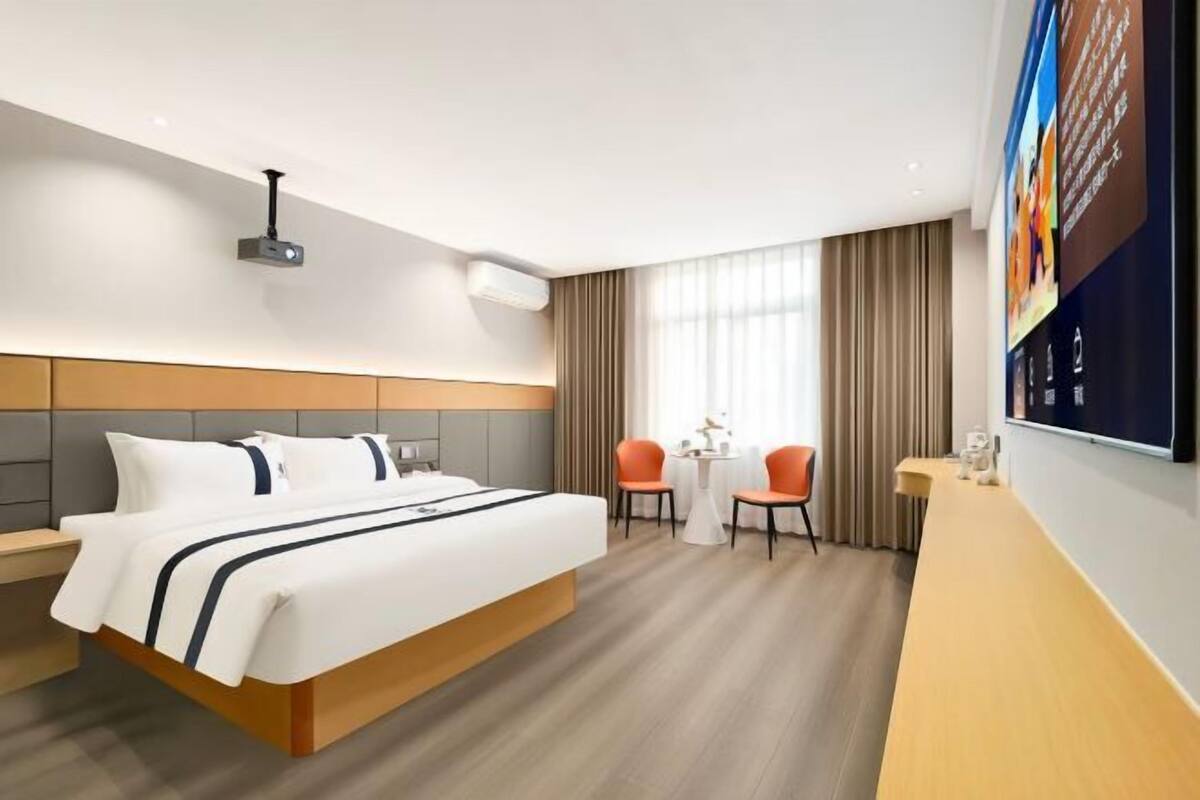 Habitación de hotel con cama, escritorio, dos sillas, televisor y ventana con cortinas.