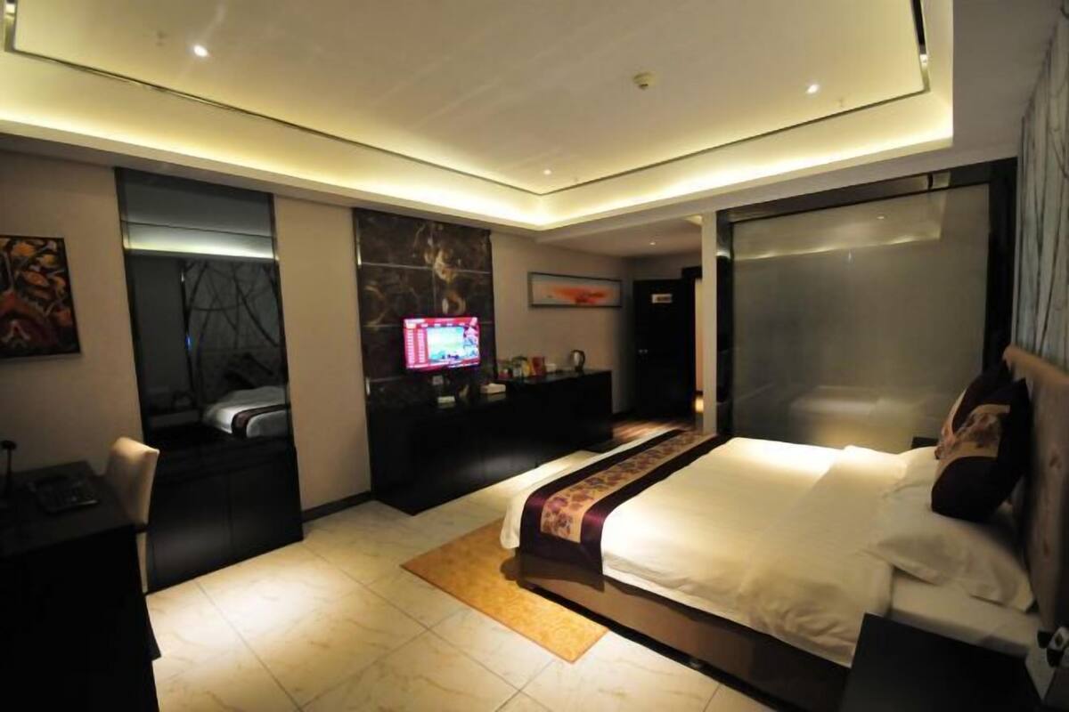 Una habitación de hotel moderna con una cama grande, un escritorio, un televisor y un baño con cabina de ducha de vidrio.