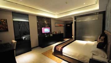 A modern hotel room with a large bed, a desk, a television, and a bathroom with a glass shower enclosure.