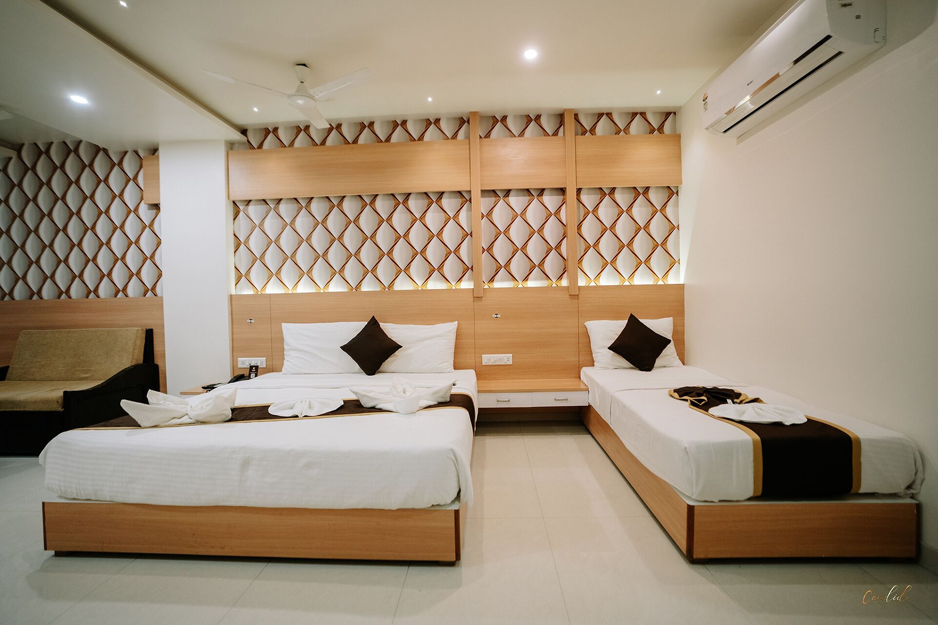A hotel room with two beds, a sofa, and a decorative wall panel.