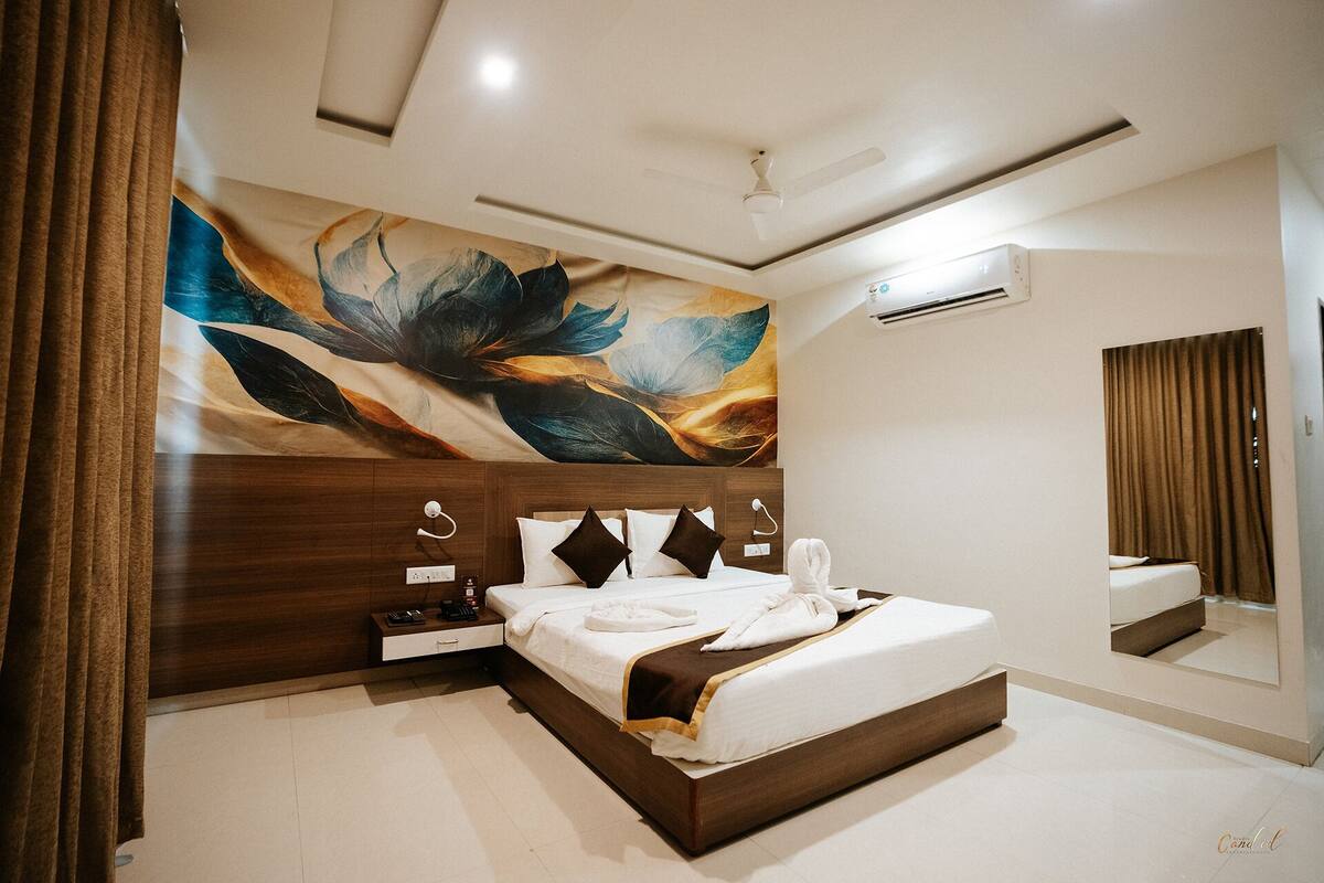 A modern bedroom with a large bed, a nightstand, a wall-mounted air conditioner, and a large abstract painting.