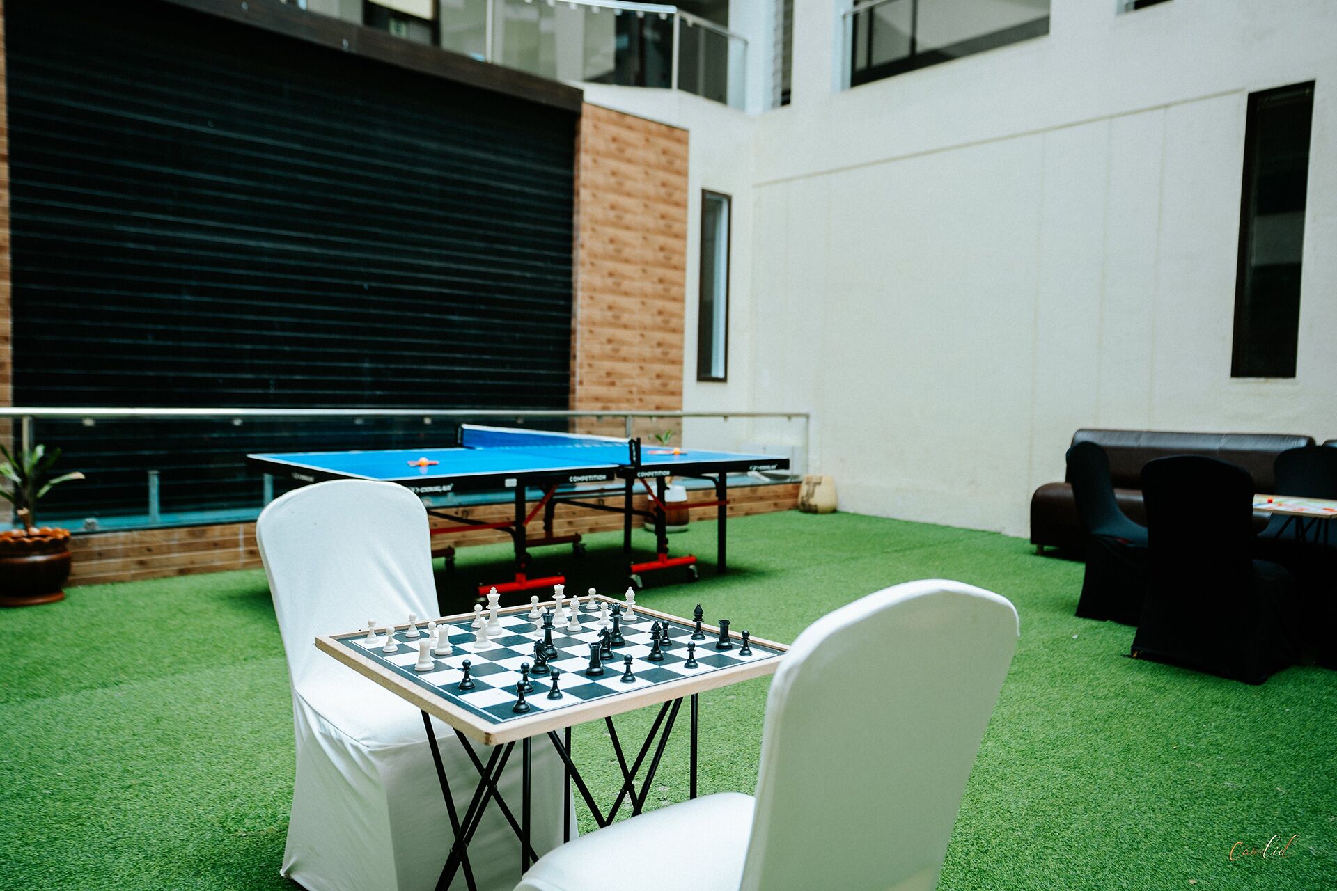 Una mesa de ping pong y una mesa de ajedrez en un espacio interior con suelo de césped artificial.