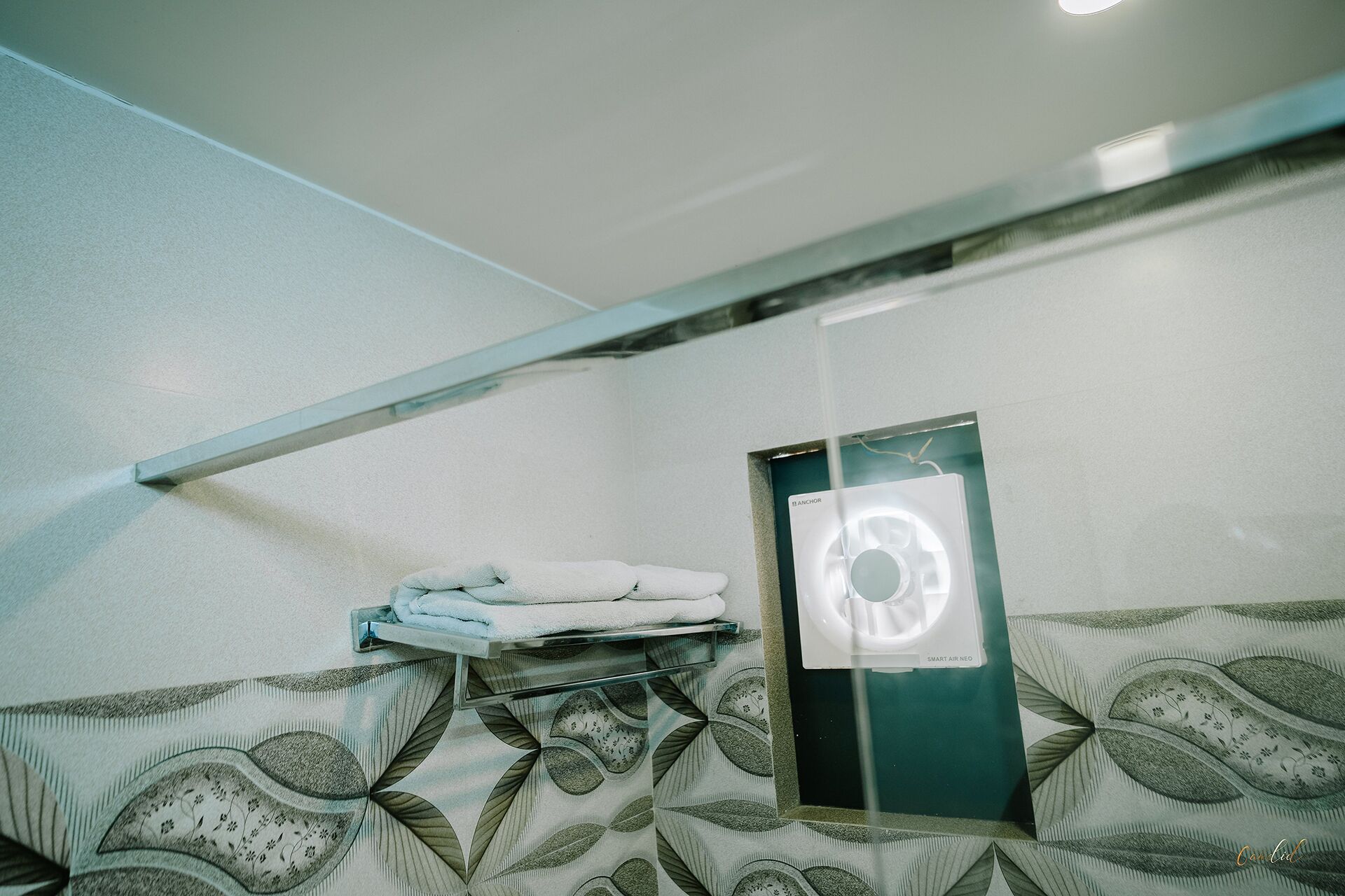 Casa de banho com um porta-toalhas, um espelho e um papel de parede estampado.