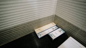 Una esquina de una habitación con pared texturizada y suelo negro. Hay tres cajas en el suelo, una de ellas con la etiqueta 'DENNA'.