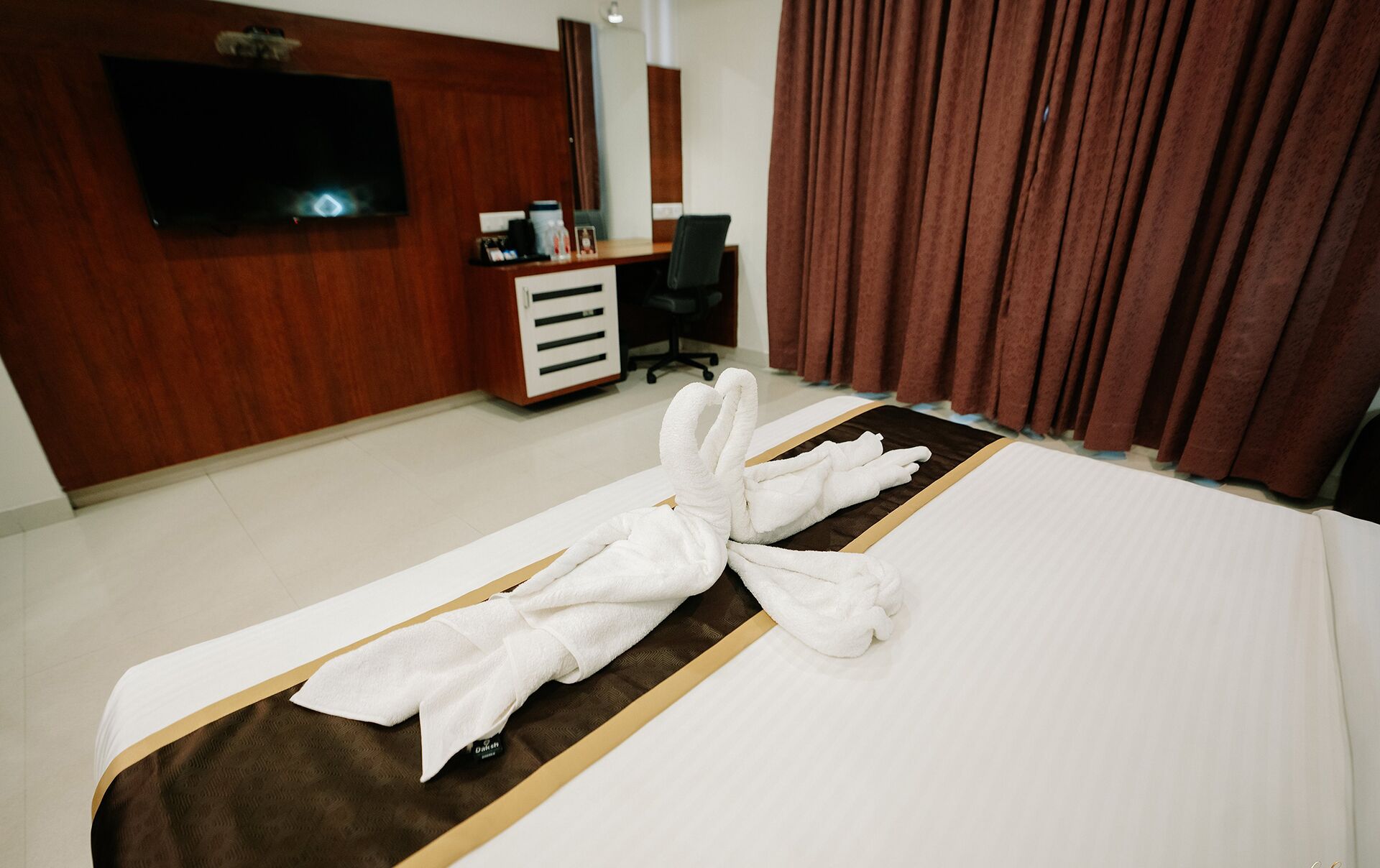 Habitación de hotel con una cama bien hecha, un televisor en la pared, un escritorio con una silla y una ventana con cortinas.
