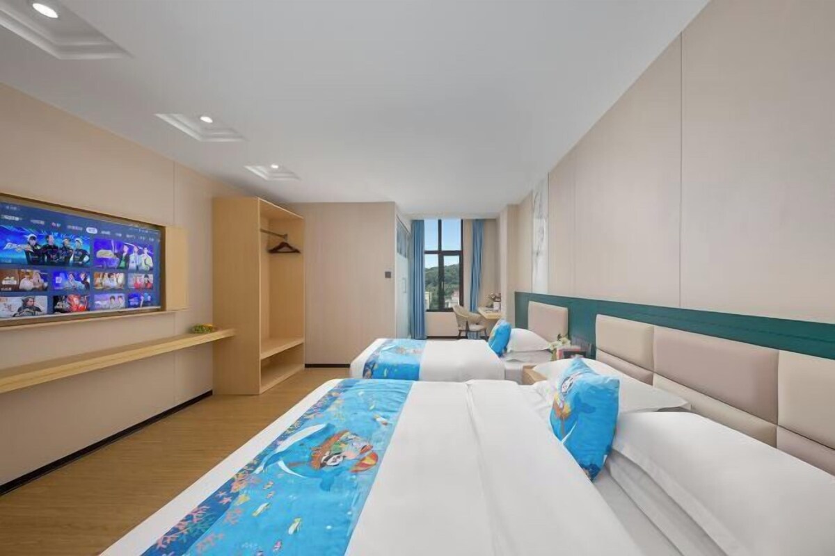 A hotel room with two beds, a TV on the wall, a wardrobe, and a window.