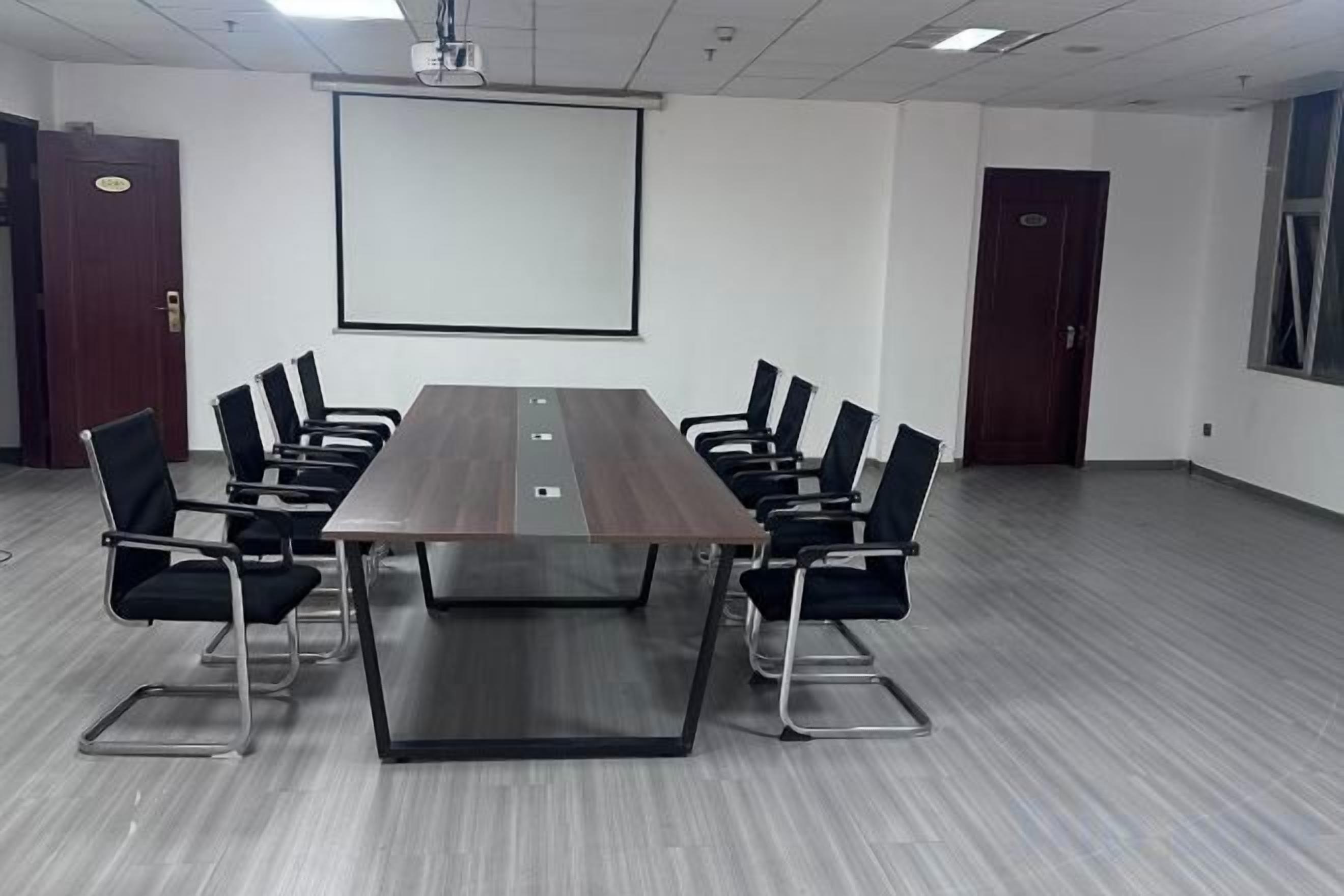 Una sala conferenze con un lungo tavolo, sedie nere, uno schermo per proiettore e una lavagna.