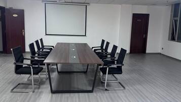 Una sala conferenze con un lungo tavolo, sedie nere, uno schermo per proiettore e una lavagna.