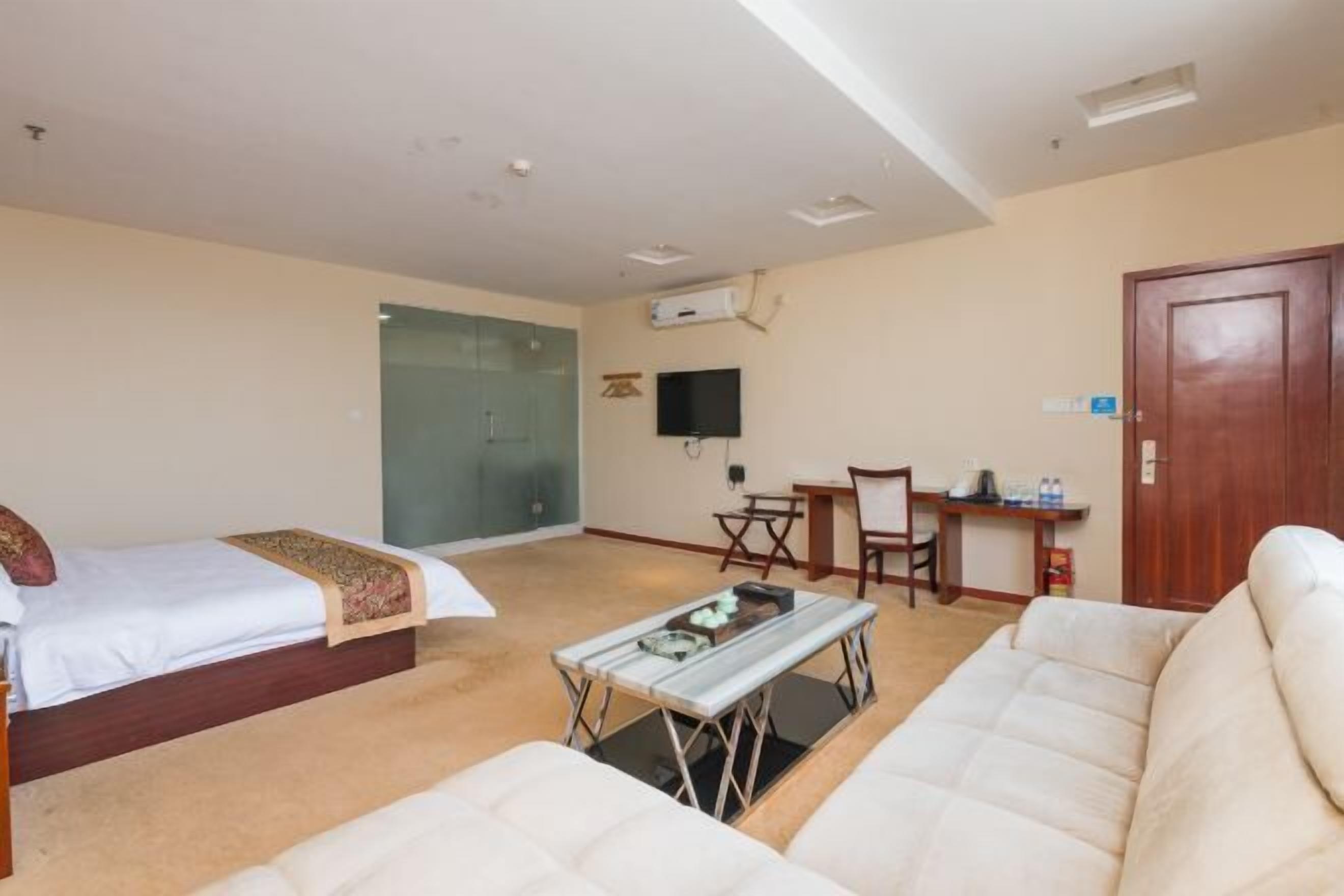 A hotel room with two beds, a sofa, a small table, a TV, and a desk.