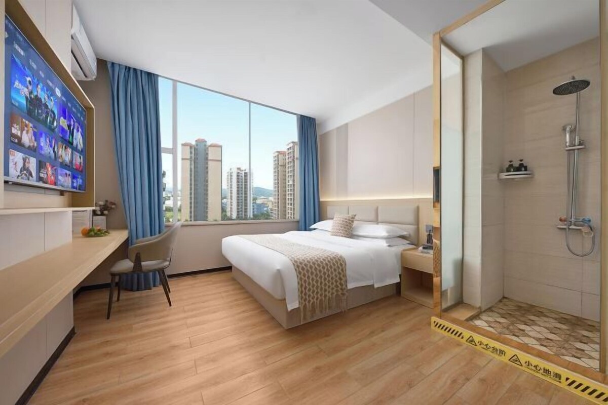 A hotel room with a bed, desk, chair, and a shower area.