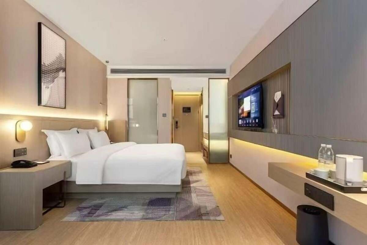 A modern hotel room with a bed, bedside table, TV, and a small desk area.