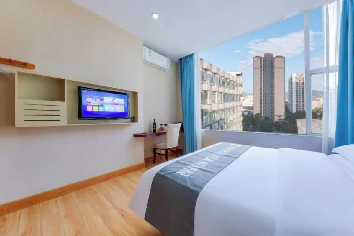 Une chambre d’hôtel équipée d’un lit, d’une télévision, d’un bureau et d’une fenêtre donnant sur la ville.