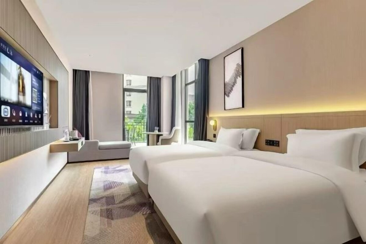 A hotel room with two beds, a TV, a desk, and a balcony view.