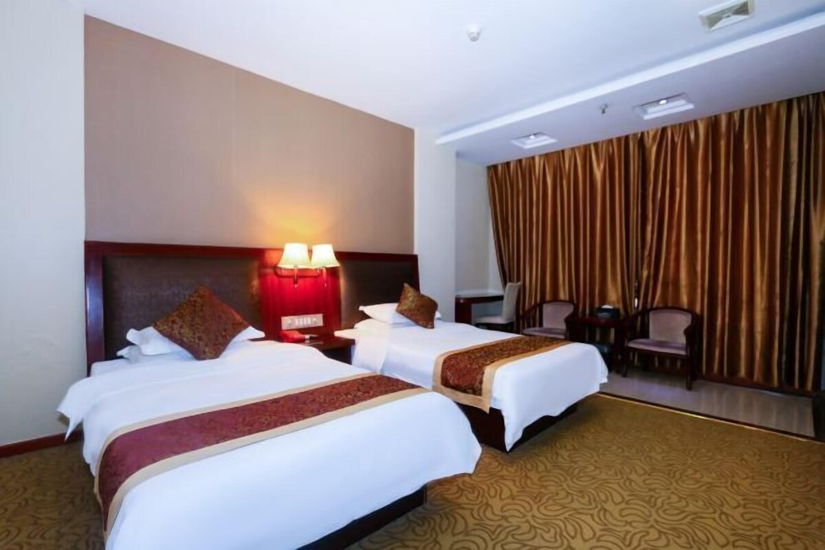 A hotel room with two beds, a headboard with a red light, a desk with a chair, and a large window with curtains.