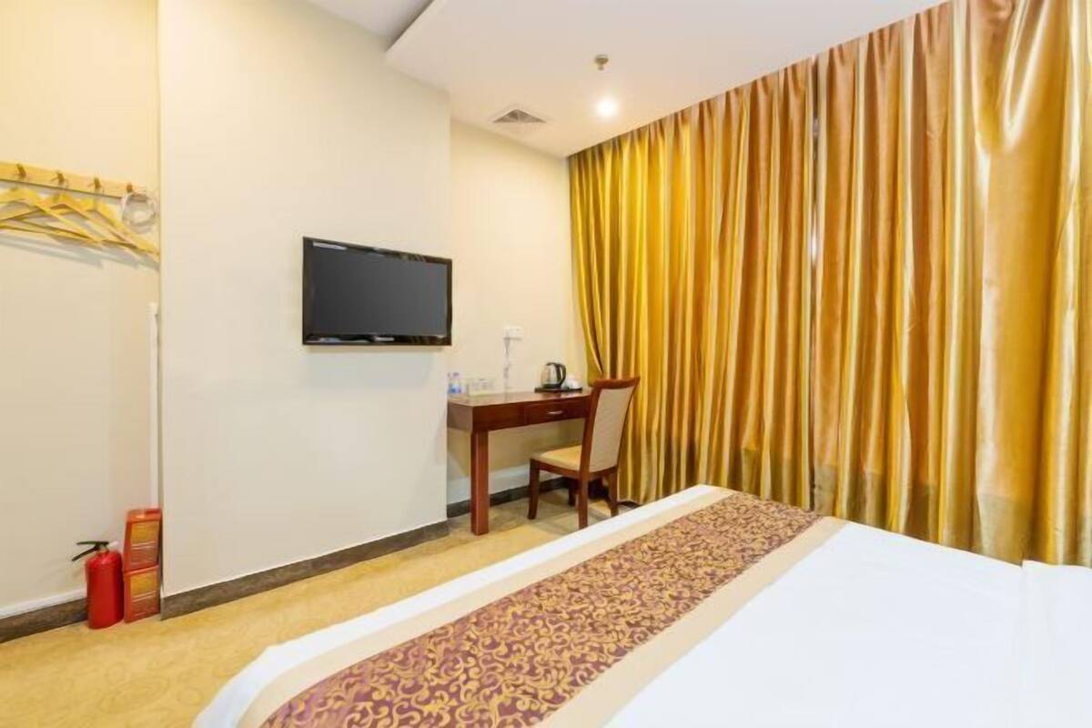 A hotel room with a bed, a desk, a chair, a television, and a curtain.