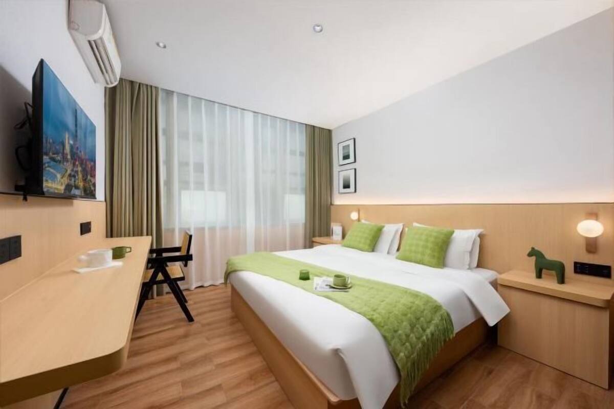 A hotel room with a bed, a desk, a chair, an air conditioner, and a painting on the wall.