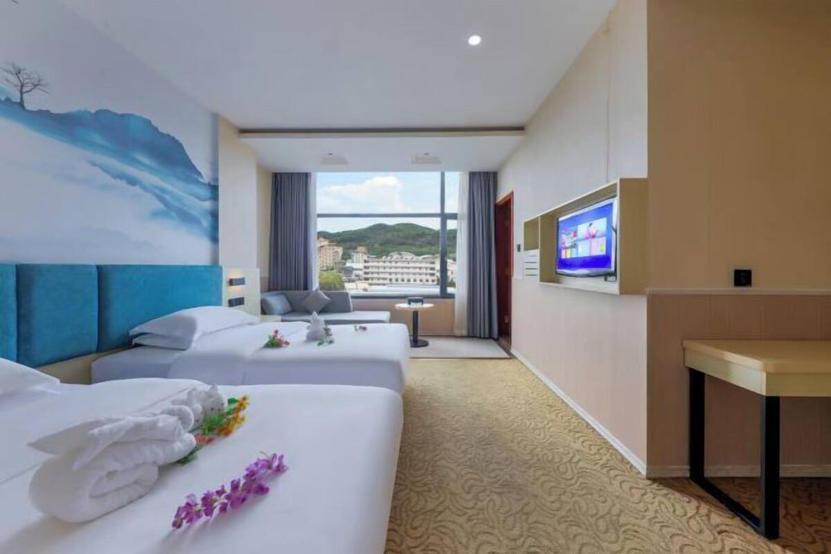 A hotel room with two beds, a TV, a small table, and a view of a cityscape.