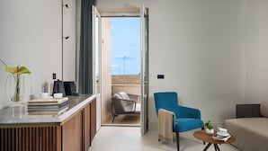 A modern hotel room with a balcony, a dining area, and a seating area with a blue chair and a sofa. -  Byssus Suites (Syracuse)
