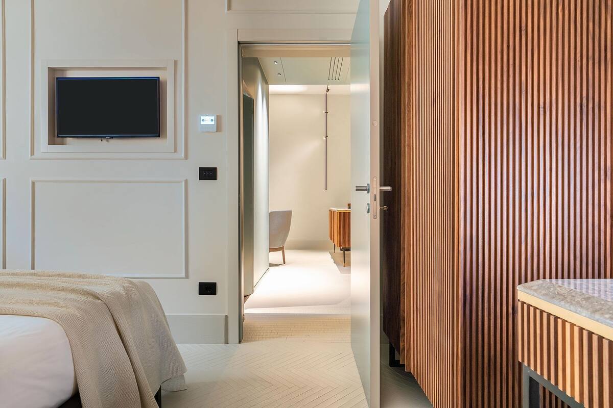 Une chambre d’hôtel comprenant un lit, un téléviseur fixé au mur, un mur recouvert de panneaux en bois et une porte donnant sur une salle de bain.