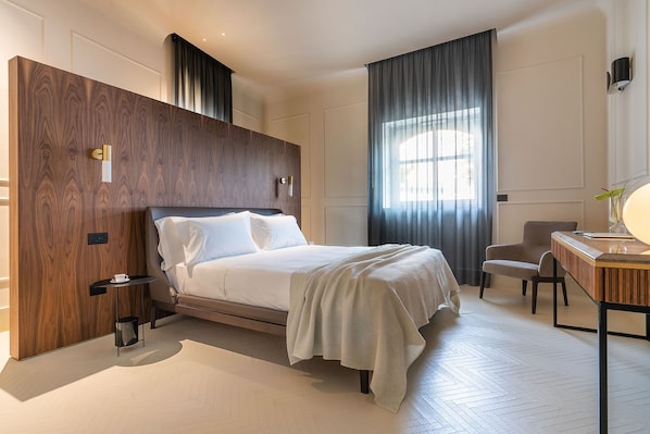 Une chambre d’hôtel moderne avec un grand lit, un bureau avec une lampe, une chaise et une grande fenêtre avec des rideaux.