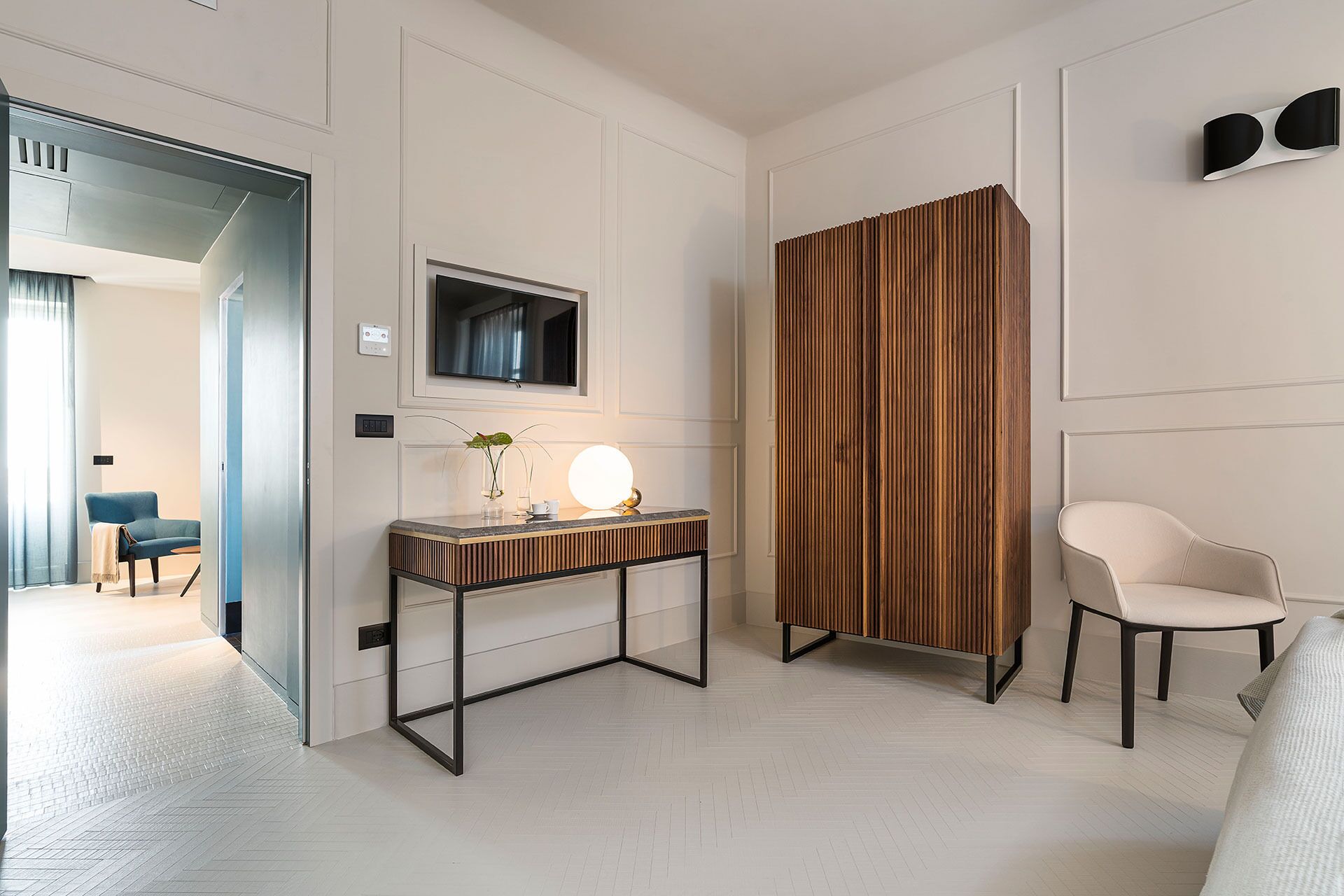 Une chambre d’hôtel moderne avec un mur d’accent en bois, un téléviseur à écran plat, une table de chevet avec une lampe et une chaise blanche.