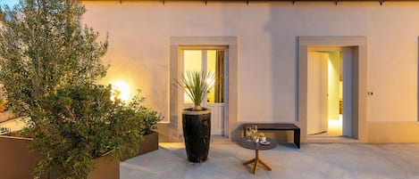 A modern outdoor patio with a concrete floor, two doors leading to interior spaces, and a small table with a vase and two glasses.