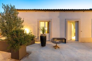 Un patio moderno al aire libre con suelo de concreto, dos puertas que dan a espacios interiores y una pequeña mesa con un florero y dos vasos.