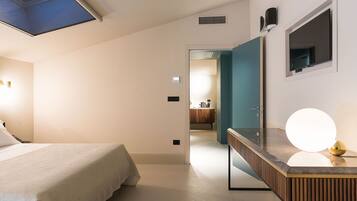Une chambre avec un puits de lumière, un lit, une coiffeuse avec un miroir et une porte donnant sur une salle de bain.