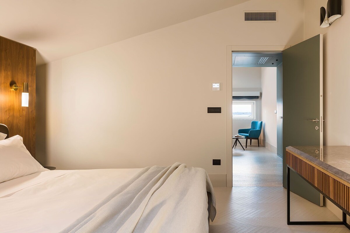 A hotel room with a bed, a wooden headboard, a mirror, a wall-mounted light, and a door leading to a bathroom.