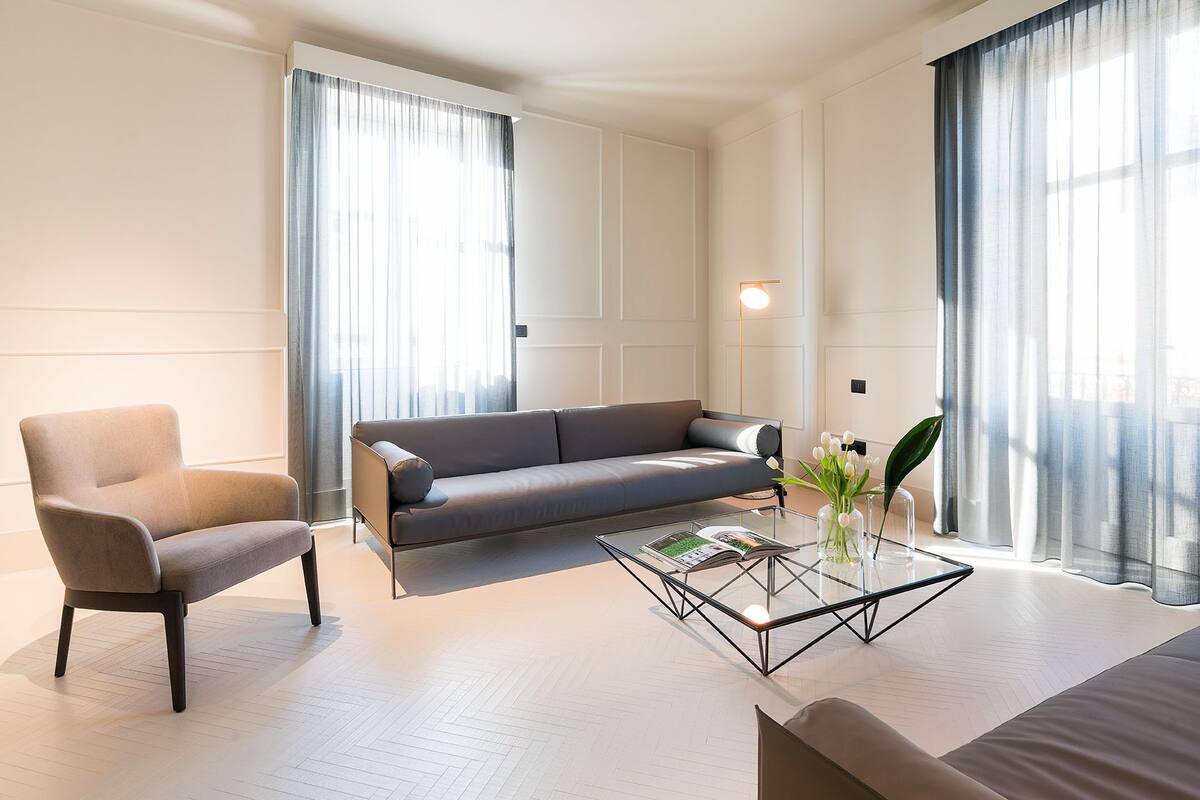 Un salon moderne avec un canapé, un fauteuil et une table basse en verre sur laquelle repose un magazine.