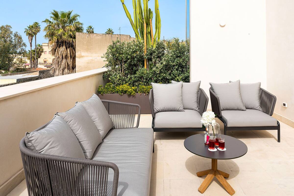Un balcon avec deux canapés gris, une petite table ronde avec des boissons et une plante en pot.