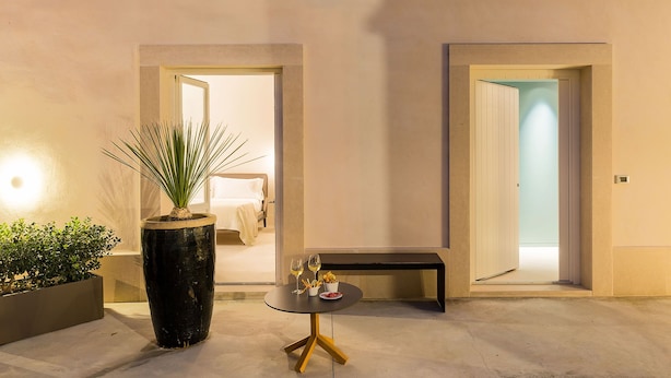 A hotel room with a bed, a small table with a glass of wine, and a potted plant. -  Byssus Suites (Syracuse)