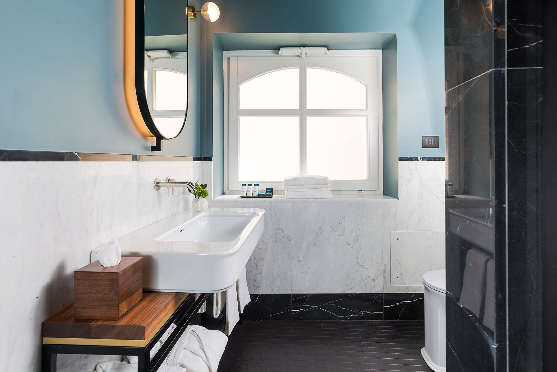 Une salle de bain moderne avec un lavabo blanc, un meuble-lavabo en bois, une grande fenêtre en arc de cercle et un espace douche noir.