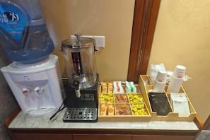 A coffee station with a water dispenser, a coffee maker, and a tray of snacks.
