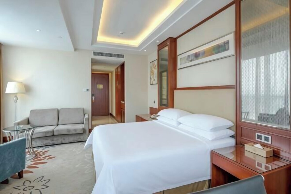 A hotel room with a bed, a desk, a chair, a sofa, and a lamp.