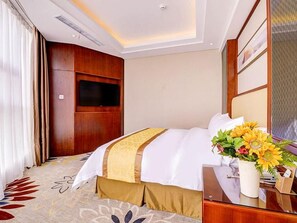 A hotel room with a bed, a television, a vase with flowers, and a wooden headboard.