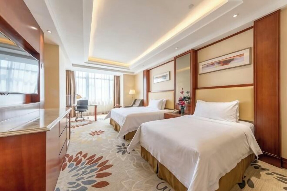 Habitación de hotel con dos camas, un escritorio, una silla y un televisor.