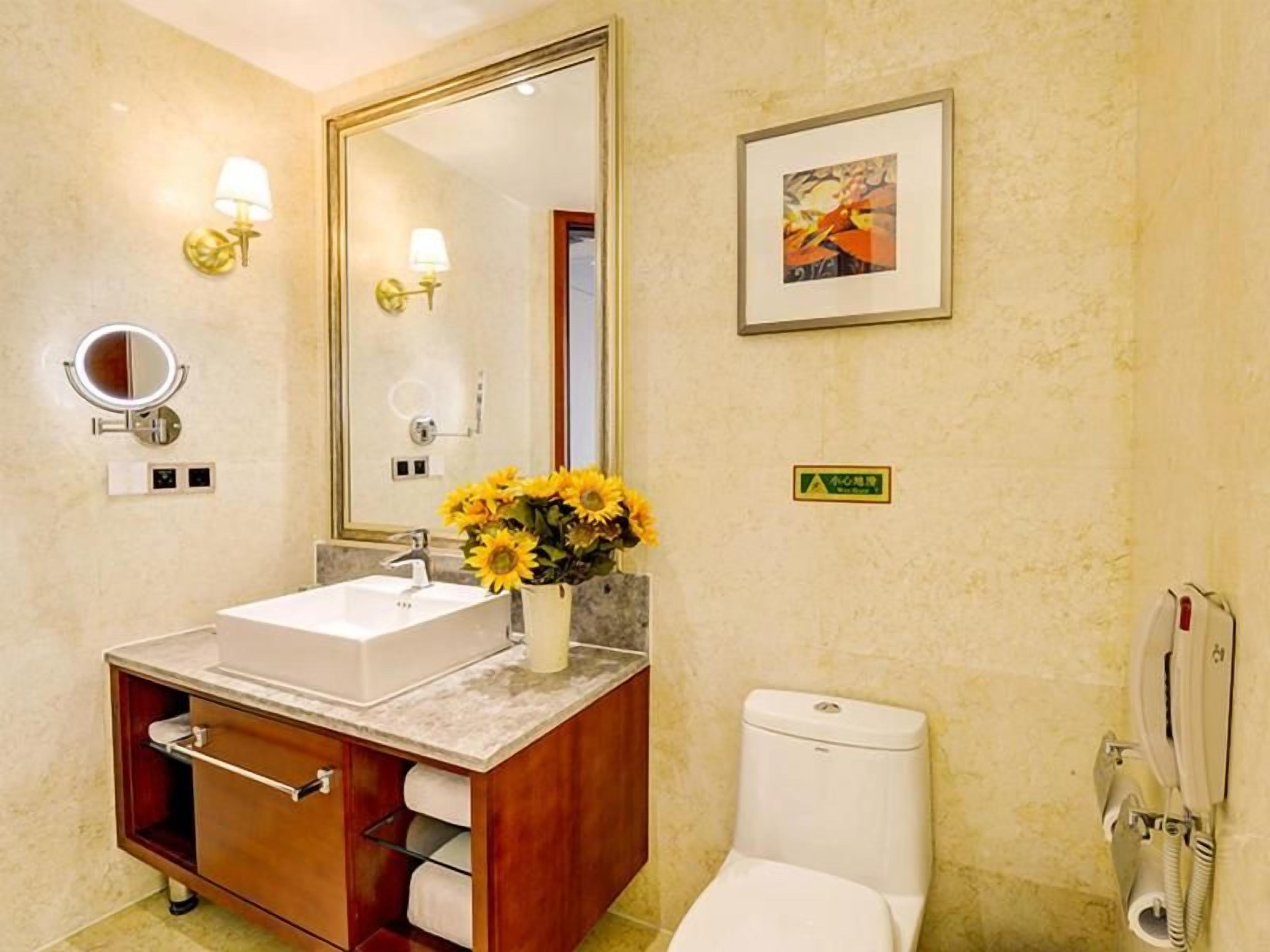 A bathroom with a sink, mirror, toilet, and a framed picture on the wall.