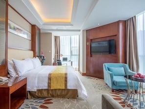 A hotel room with a bed, a TV, a blue armchair, and a small table with fruit. - Vienna Hotel (Nanchang County Chengbi Lake) (Nanchang)