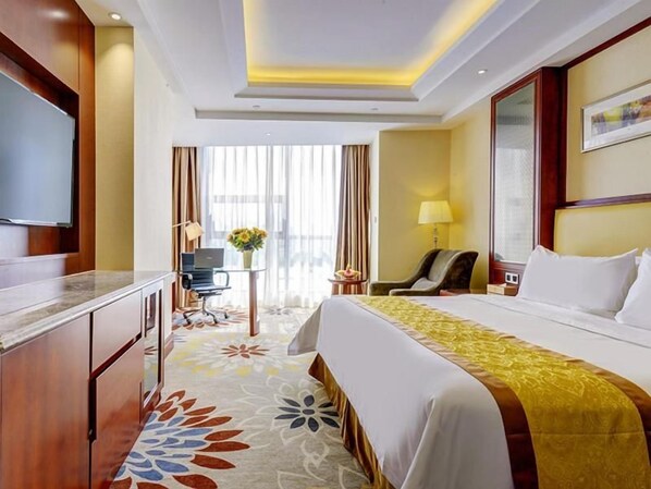 Habitación de hotel con cama, escritorio, silla, televisor y ventana con cortinas.