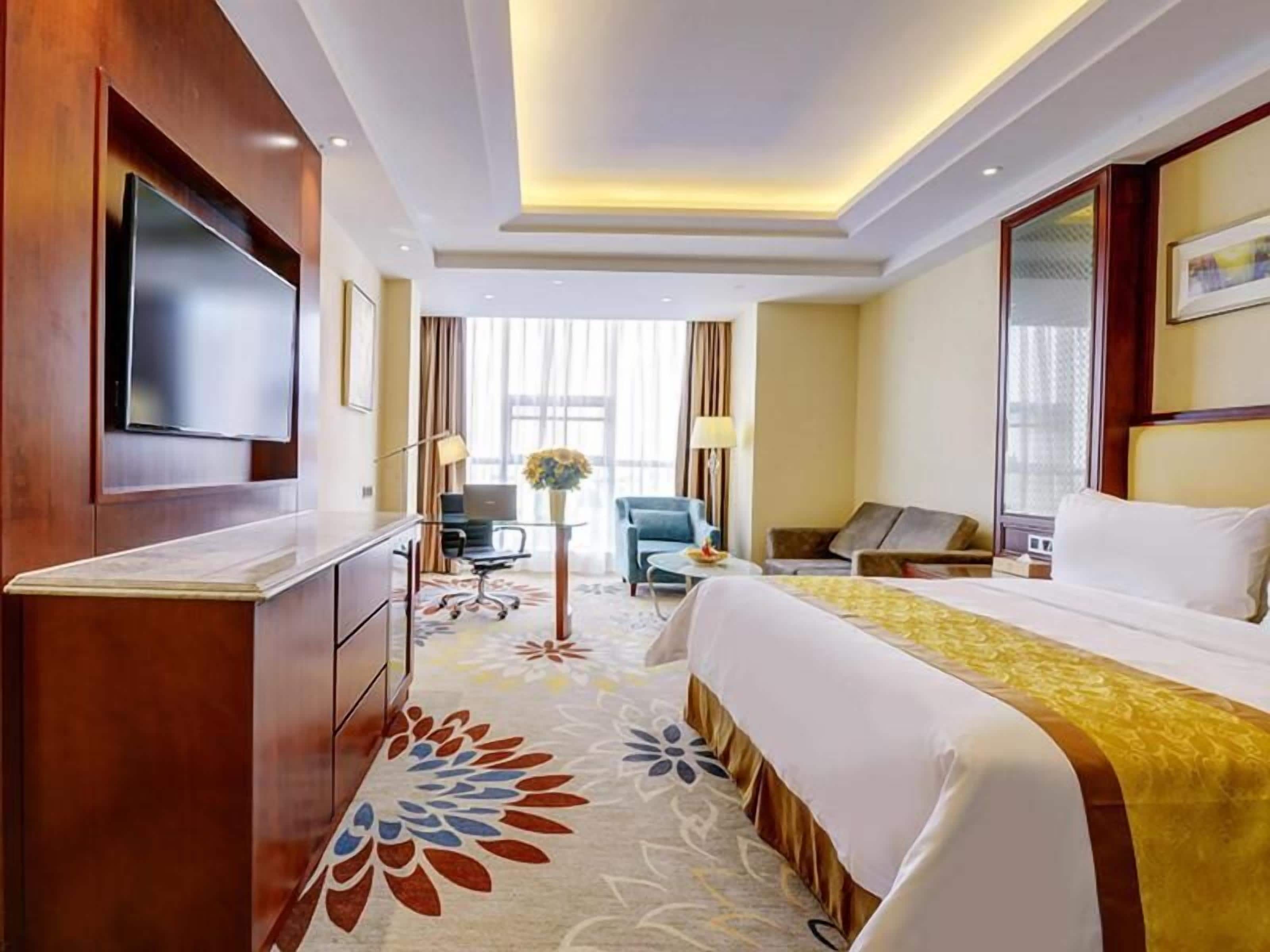 A hotel room with a bed, a desk, a TV, and a chair.