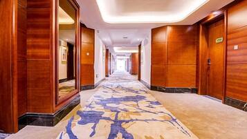Un pasillo de hotel con paredes de madera, alfombra estampada y un largo camino hacia una puerta al final.