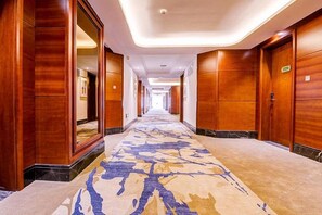 A hotel corridor with wooden walls, a patterned carpet, and a long hallway leading to a door at the end.