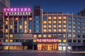 A hotel with multiple floors, a prominent entrance, and illuminated signage. - Shiwai Taoyuan Eco Hotel (Huaihua)