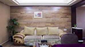 A living room with a wooden wall, a sofa, a glass coffee table, and a chair. - Shiwai Taoyuan Eco Hotel (Huaihua)