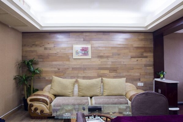 A living room with a wooden wall, a sofa, a glass coffee table, and a chair. - Shiwai Taoyuan Eco Hotel (Huaihua)