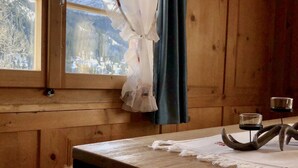 Ein Holzhütten-Zimmer mit Fenster, einem Tisch und einem Kerzenhalter sowie einem Fellteppich.