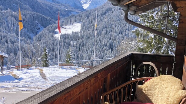 Ein hölzerner Balkon mit Blick auf schneebedeckte Berge und Flaggen.